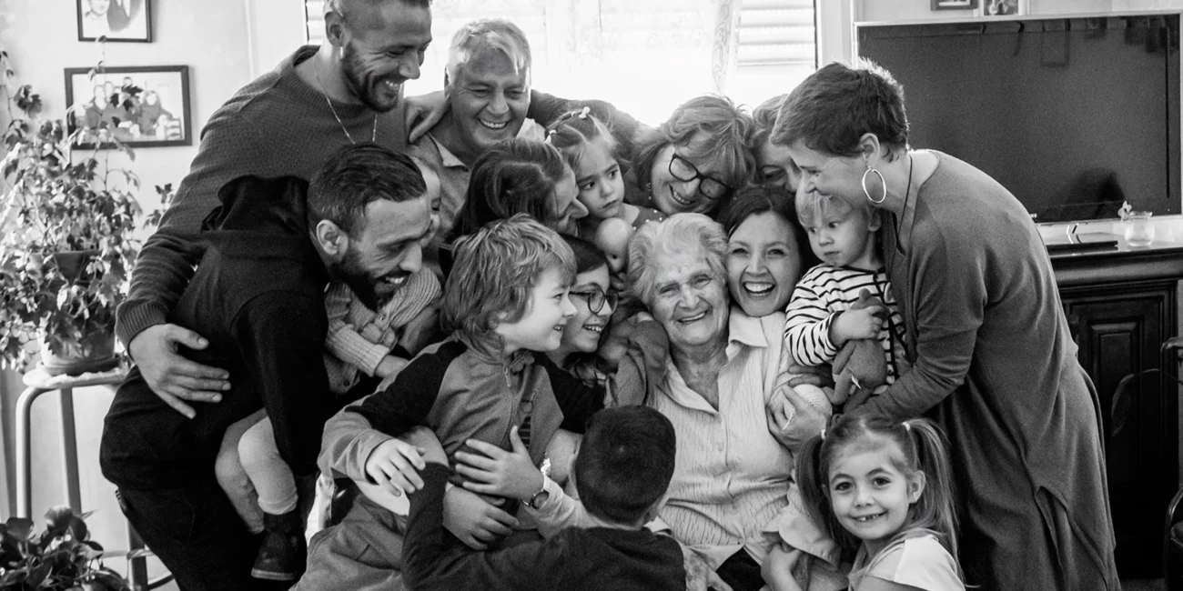 Photo noir et blanc d'une famille plusieurs personne font un gros câlin à leur grand-mère qui sourit de bonheur